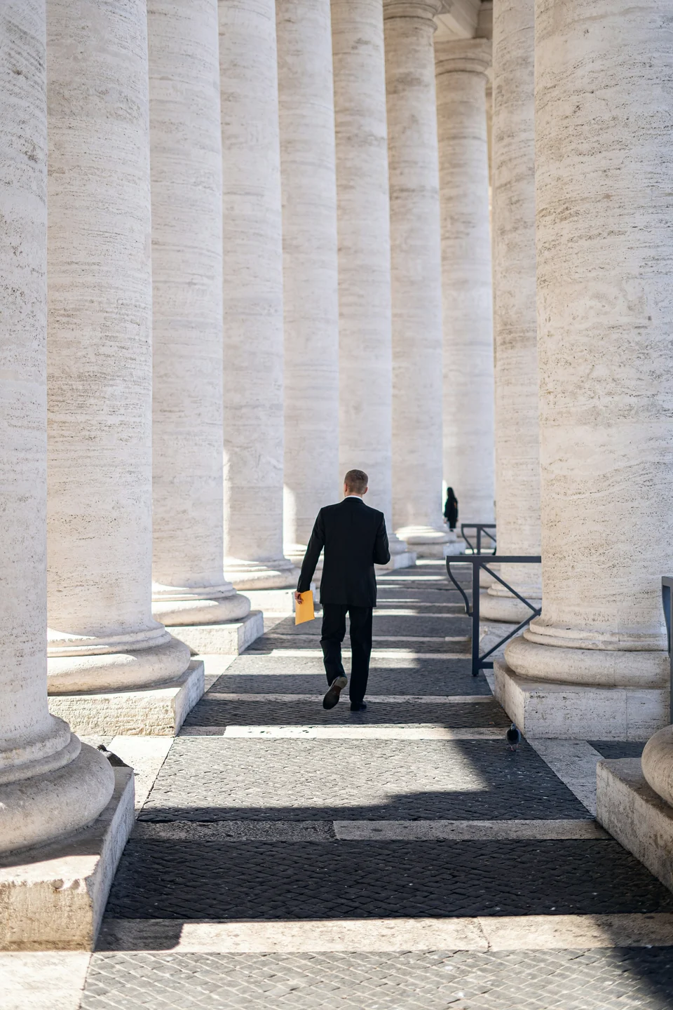 A man walking through a stone colonnade