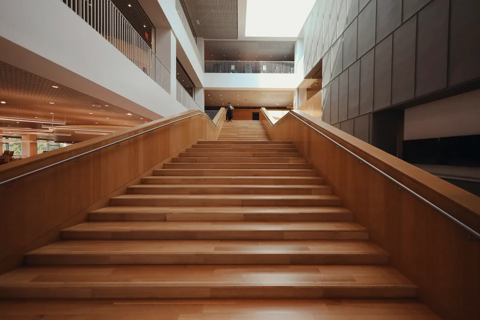 A broad wooden staircase rising through a library