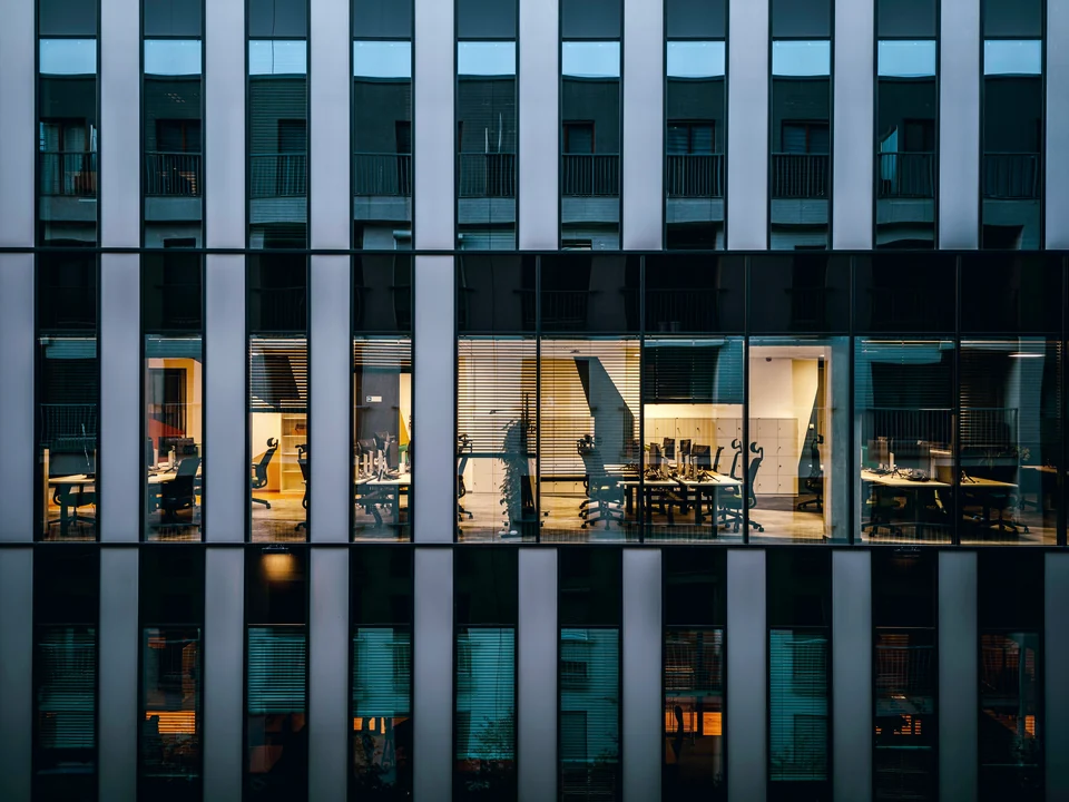 Lit office windows behind a building's facade at dusk
