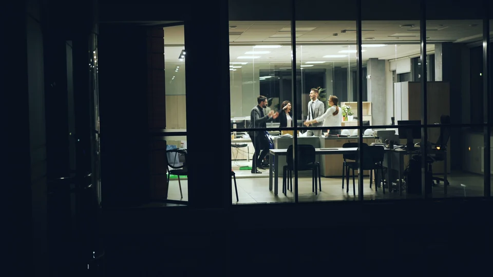 An office seen through its windows at night, with a team gathered inside